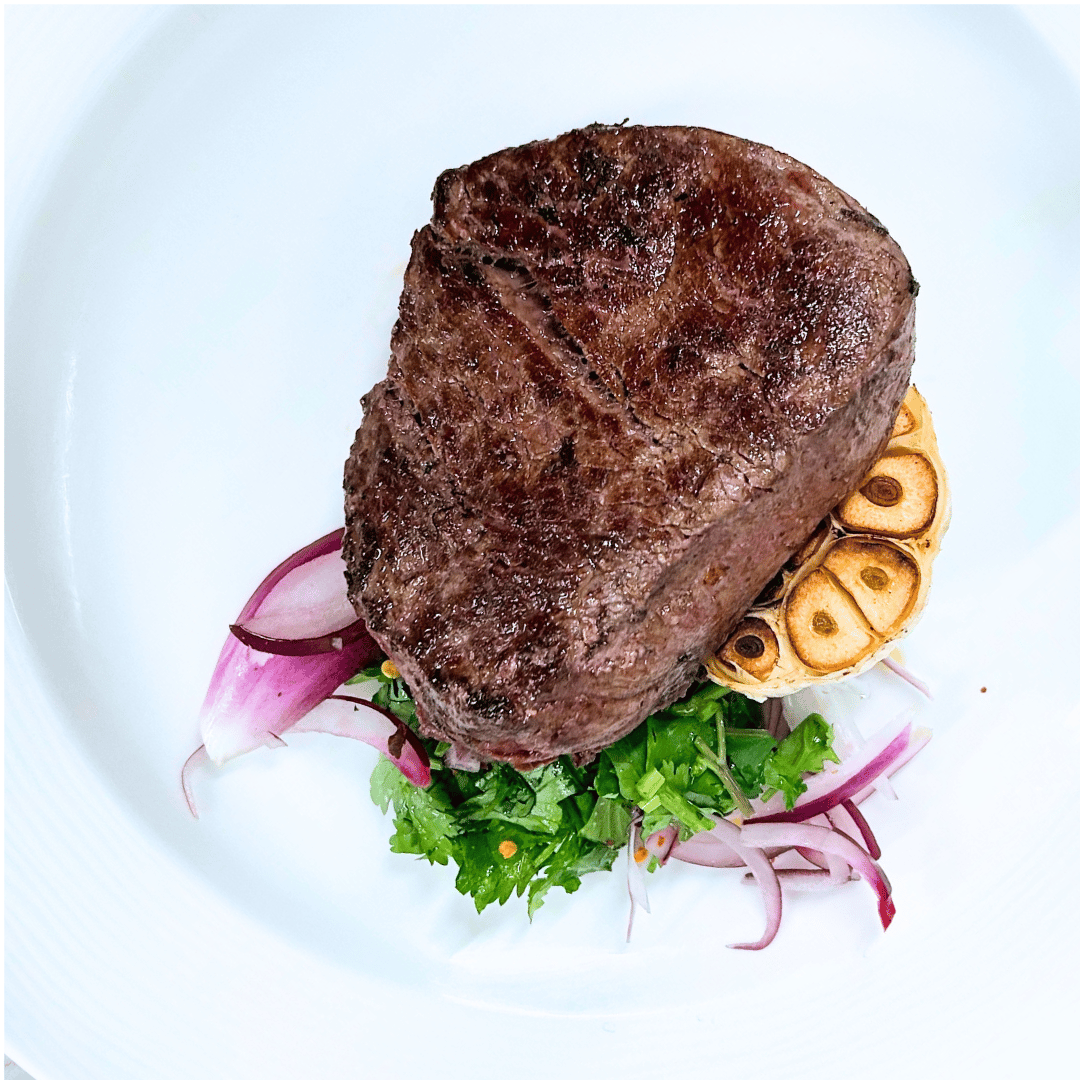 Bison filet steak plated with garlic, herbs and shallots.
