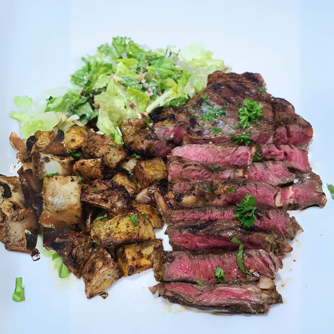 Bison ribeye steak carved and plated with crispy herbed potatoes and crispy fresh salad.