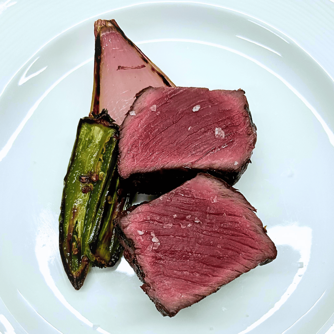 Bison sirloin steak cut and plated with flaky salt, shallots and some green peppers.